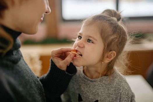 A parent feeding a young girl a piece of fruit in a cozy home setting.